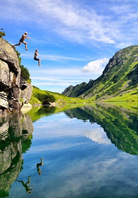 Young,Couple,Jump,Together,Into,Lake,In,Mountains,With,Beautiful